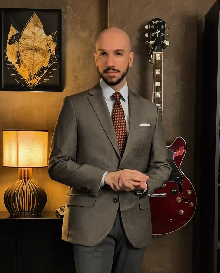 Foto de um homem que personifica o ápice da elegância, do peitoral para cima, vestindo um terno azul marinho e gravata, com postura de confiança e sofisticação.